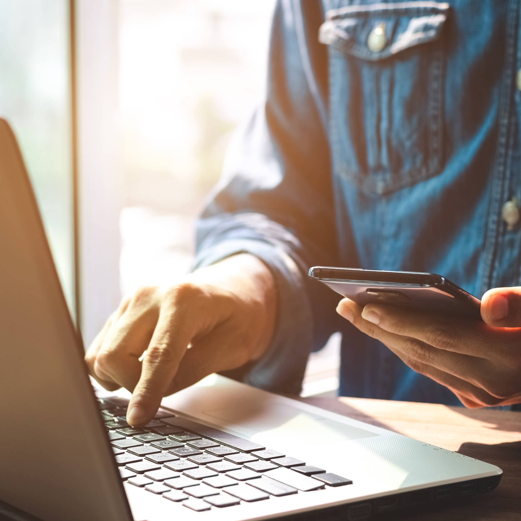 Person typing on laptop keyboard with phone in hand