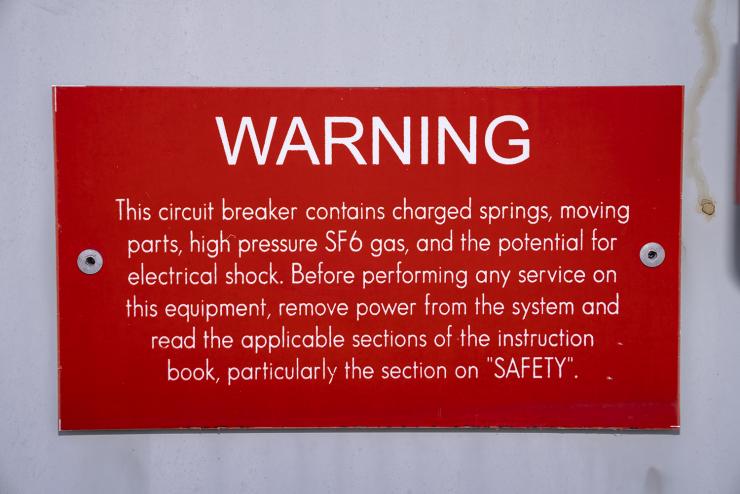 A warning sign on a high-voltage circuit breaker mentioning sulfur hexafluoride (SF6). SF6 has a global warming potential 23,900