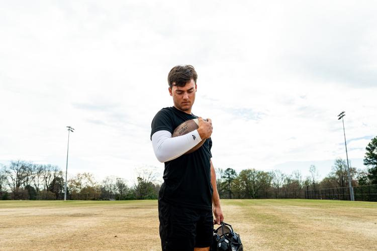 Football player holding a football while wearing a white VETTEX performance arm sleeve on an outdoor field.