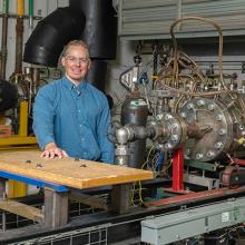 Benjamin Emerson stands with the high pressure liquid sprays combustor rig that his team uses to test novel combustor concepts.